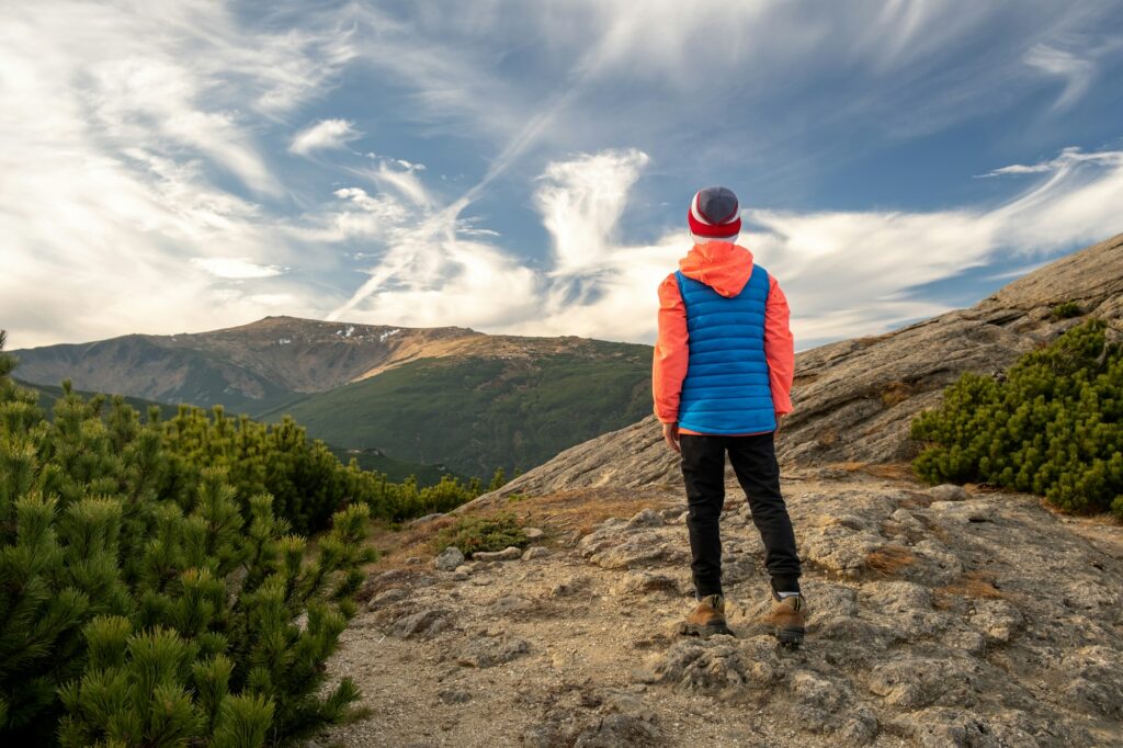 Young child boy hiker standing in mountains enjoying view of amazing mountain landscape